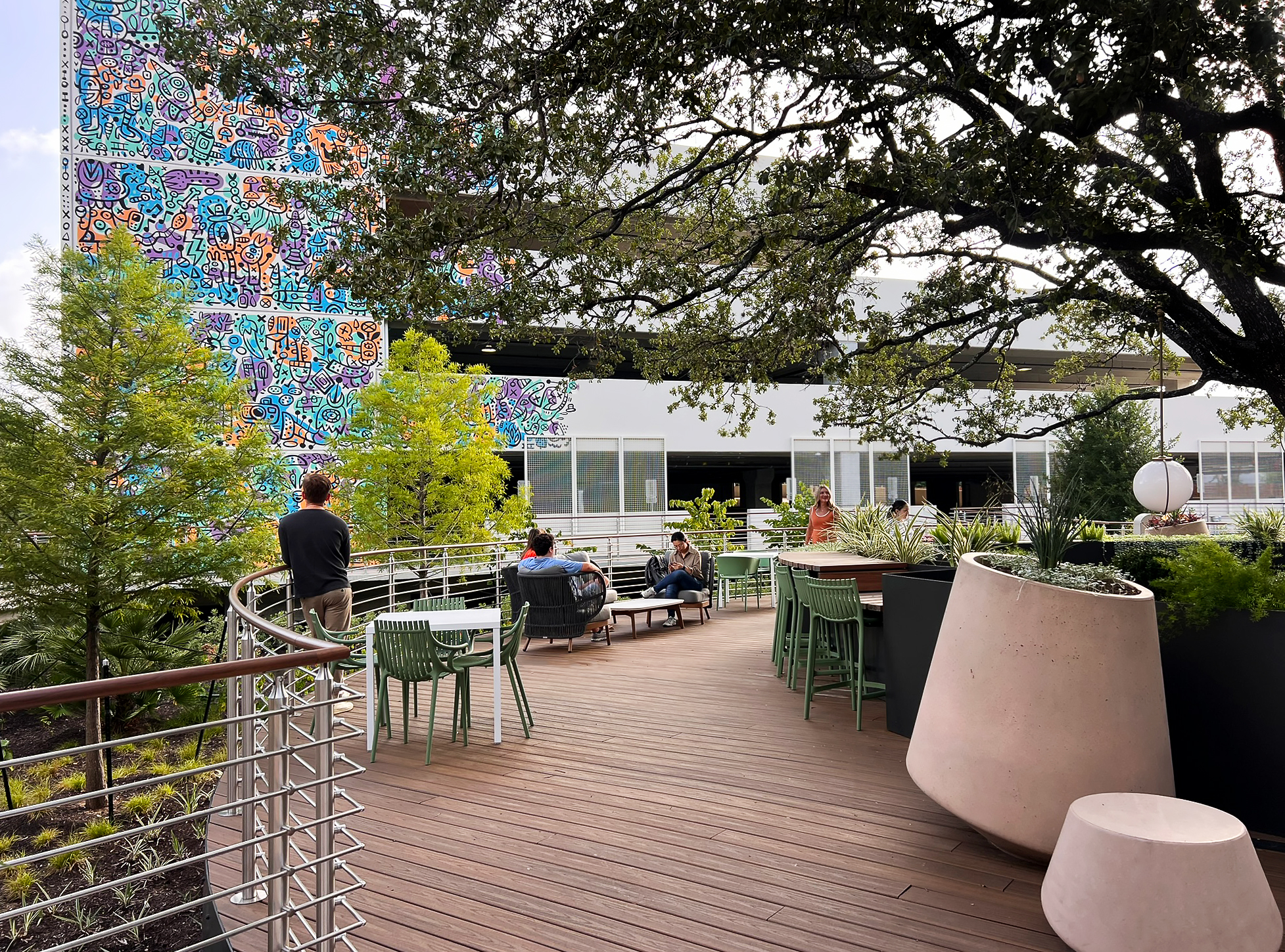 The deck in use — tables and chairs beneath the oak, the mural facade beyond