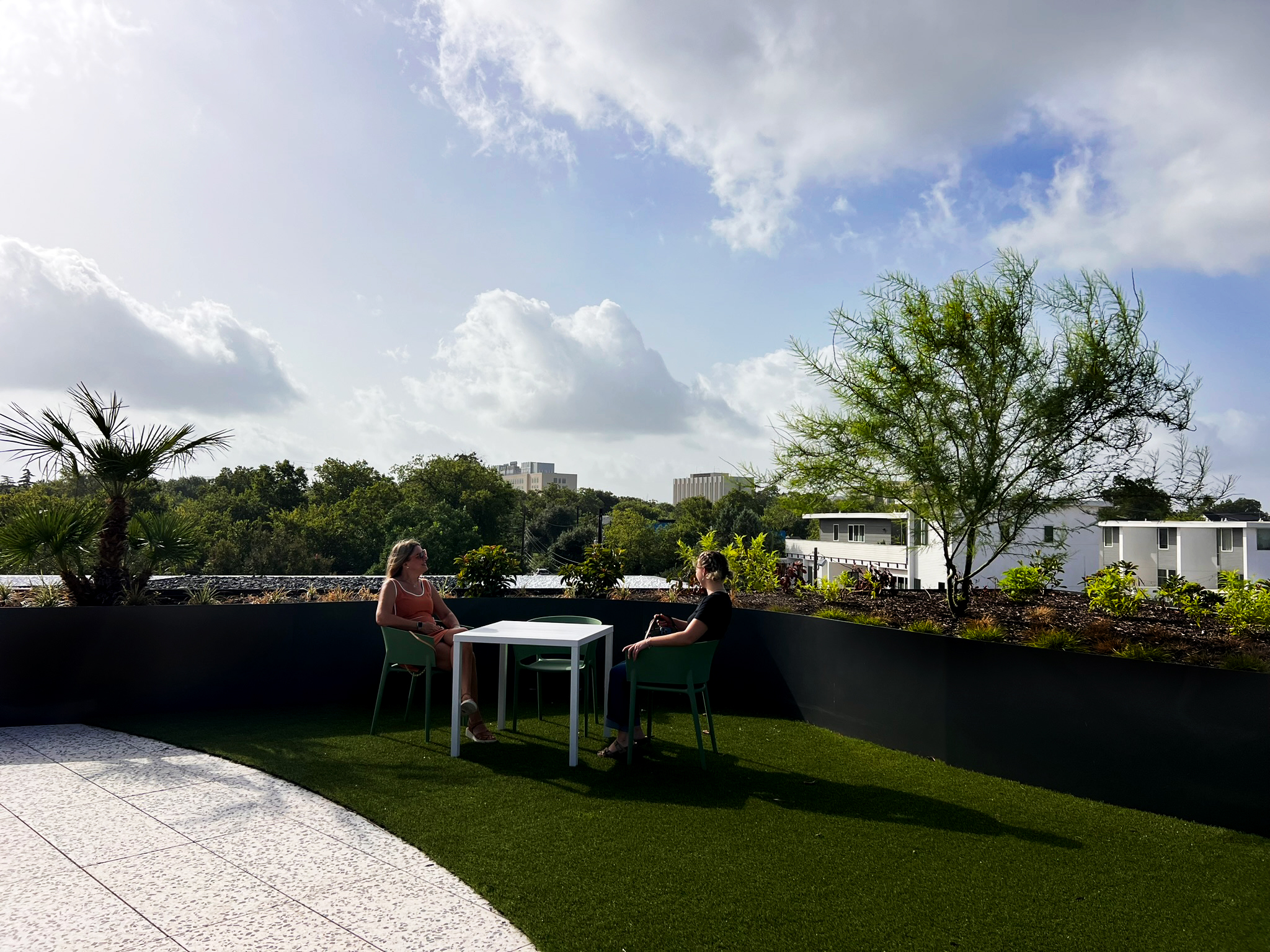 Two people at a table on the turf terrace, planted parapet and city beyond