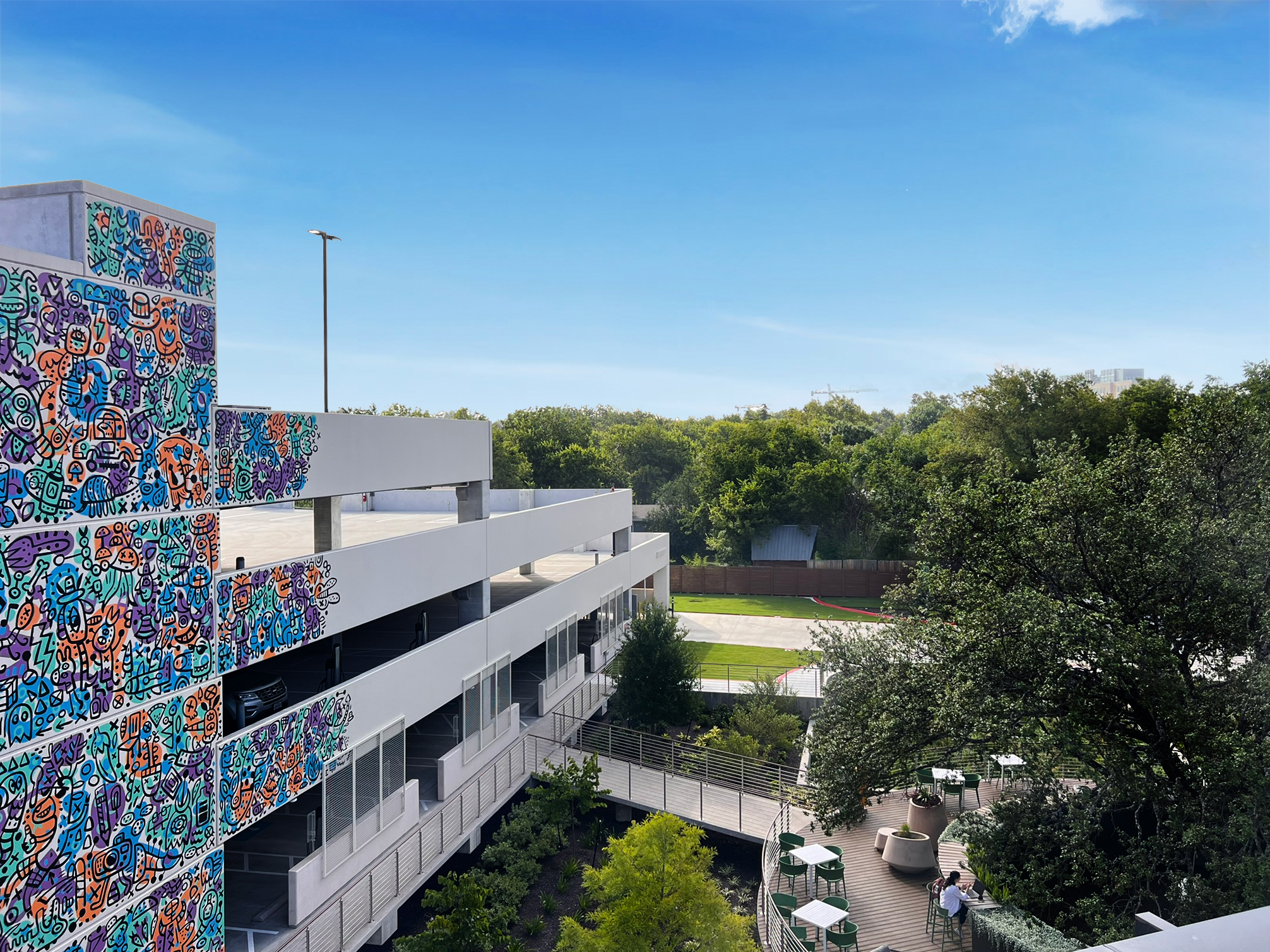 Aerial view over the muralled parking structure toward the deck and tree line
