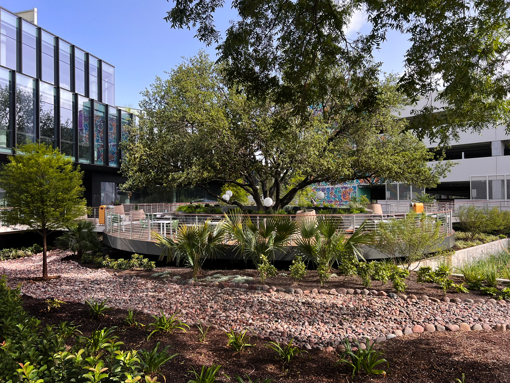 The oval deck seen across a river-rock swale and mixed shrub planting